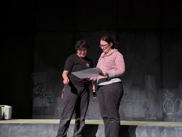 Two people stand on a stage reviewing a lighting plan