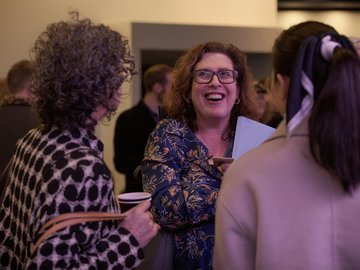 Woman laughing, glasses, floral print dress, chatting in a crowd.
