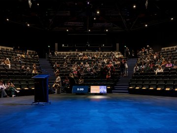 Auditorium with attendees, stage with lectern, and countdown timer.