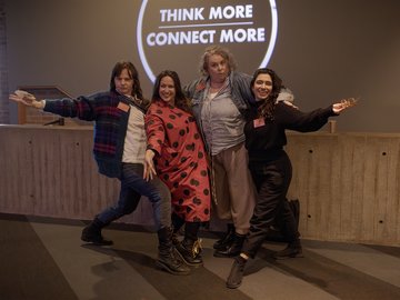 Four women posing playfully in front of a screen with 'Think More Connect More.