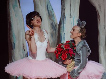 A woman with glasses, wearing a tutu, and another woman dressed as a kangaroo, wearing a tutu and holding a bunch of red roses.
