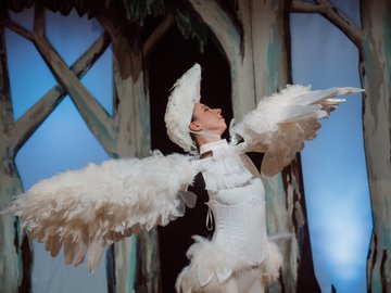 A woman dressed as a white bird, holding her arms out as wings.