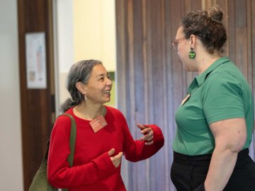 Two women smiling in a meeting with one wearing a green top, other wearing a red top.