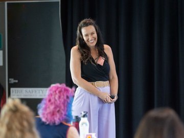 Woman smiling on stage wearing pale purple pants.