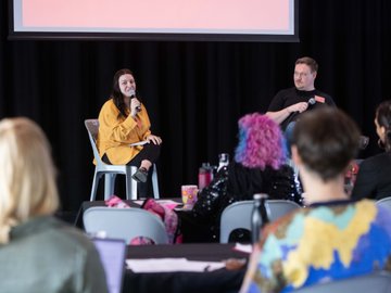 Two speakers, one with a microphone, addressing an audience; stage presentation.