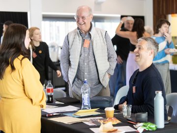 Informal networking event, people chatting around a table with refreshments at a conference.