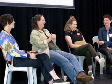 A panel of four women on stage smiling during a conference session. 