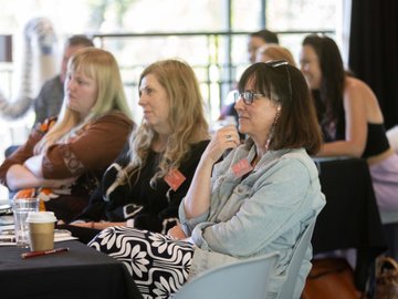 Conference attendees listening to a speaker, taking notes, and drinking coffee.