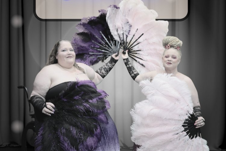 Two individuals in feathered costumes hold large, ornate fans in front of a dark, curtained background.