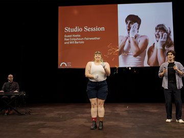 A large screen displays the title "Studio Session". A person in the centre, wearing a white tank top, navy shorts, boots, and white gloves, is holding a party popper, from which colourful confetti is exploding.