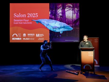 Salon 2025 event with speaker and whale puppet performance on stage.