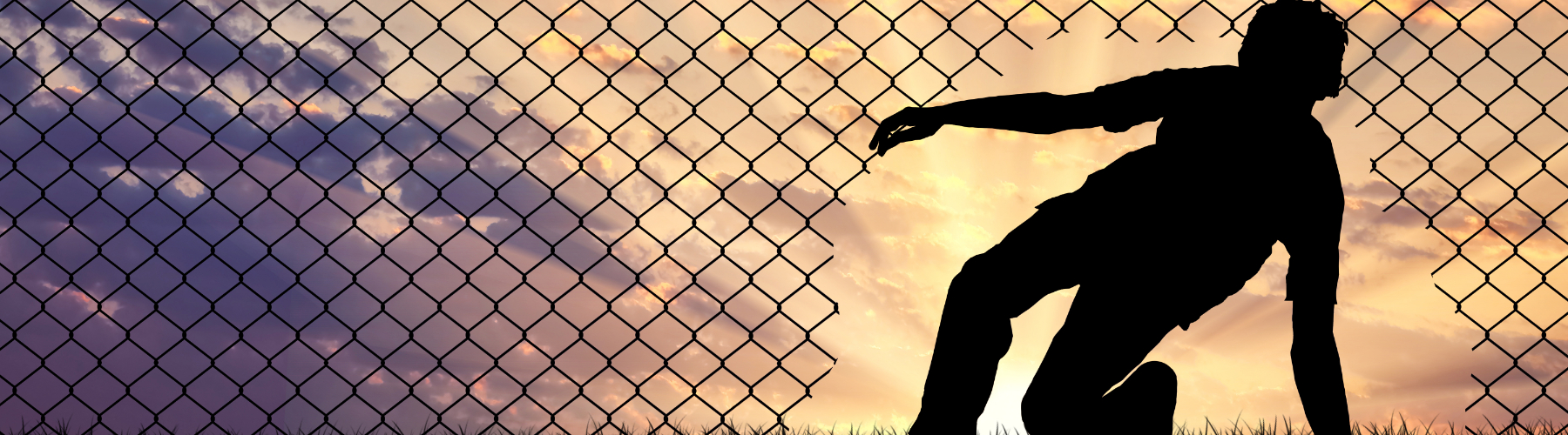 Silhouette of a person crawling through a hole in a chain-link fence, with a sunset in the background.