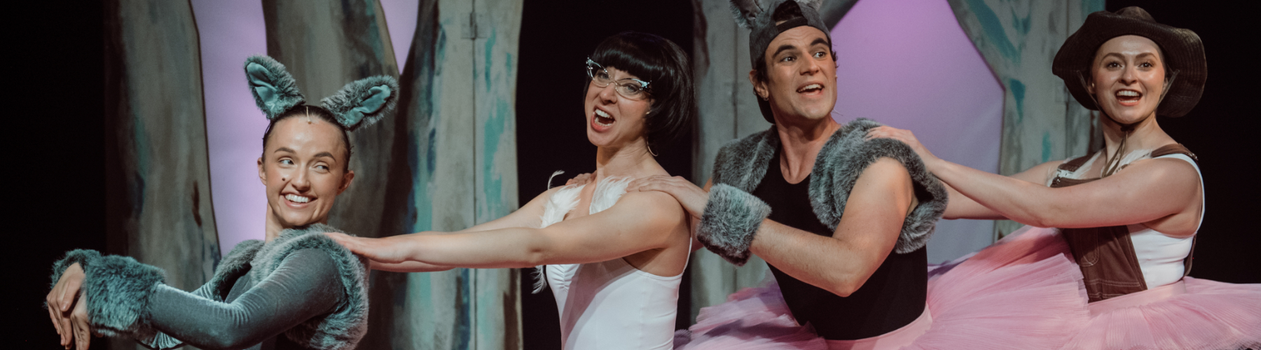 Four people singing and dancing in a row, wearing tutus. Two are dressed as kangaroos.